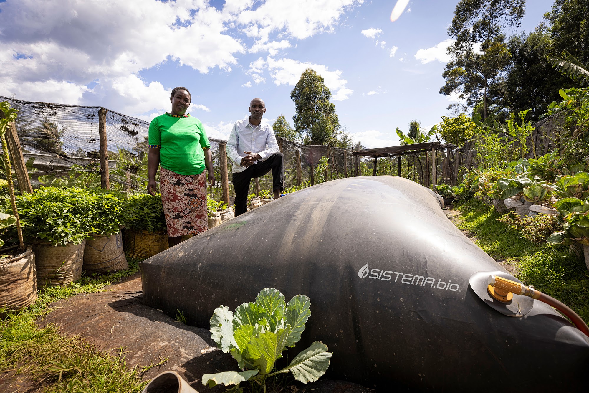 Smallholder farmers, a couple, standing beside their Sistema.bio biodigester.